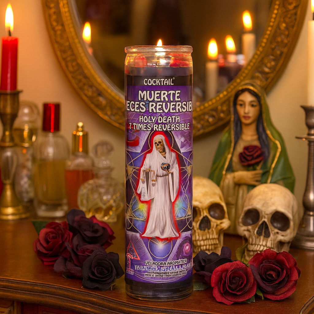 Candle labeled 'Muerte Eces Reversible' on a table with roses, skulls, and a mirror in the background.