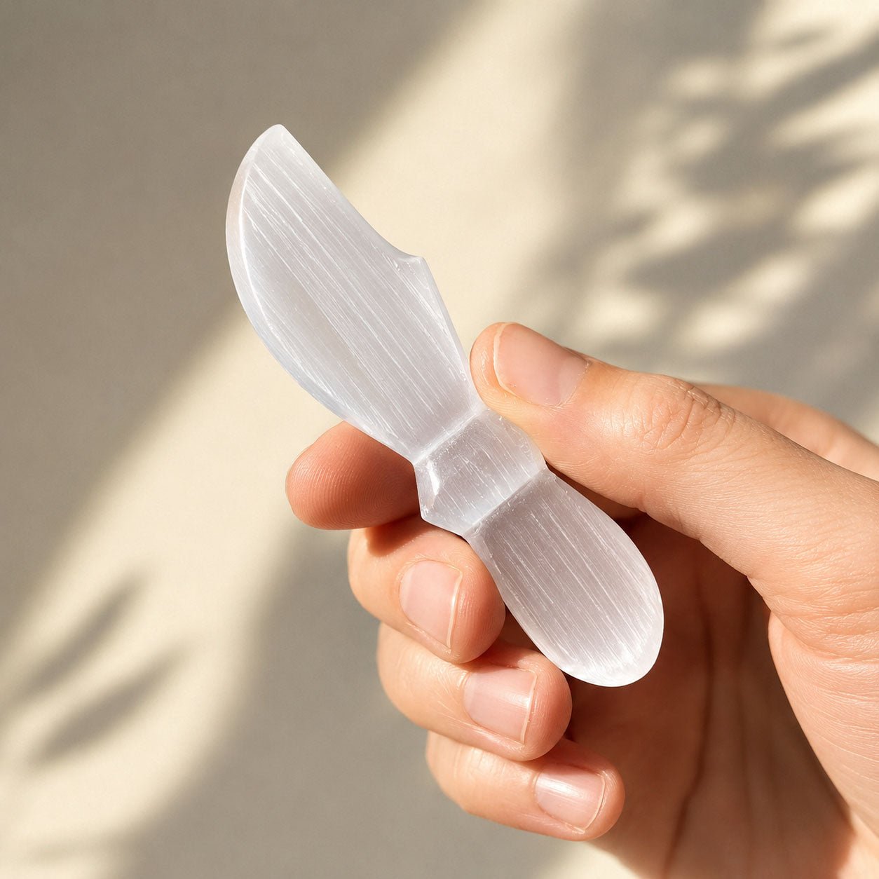 Selenite knife held in a hand against a neutral background