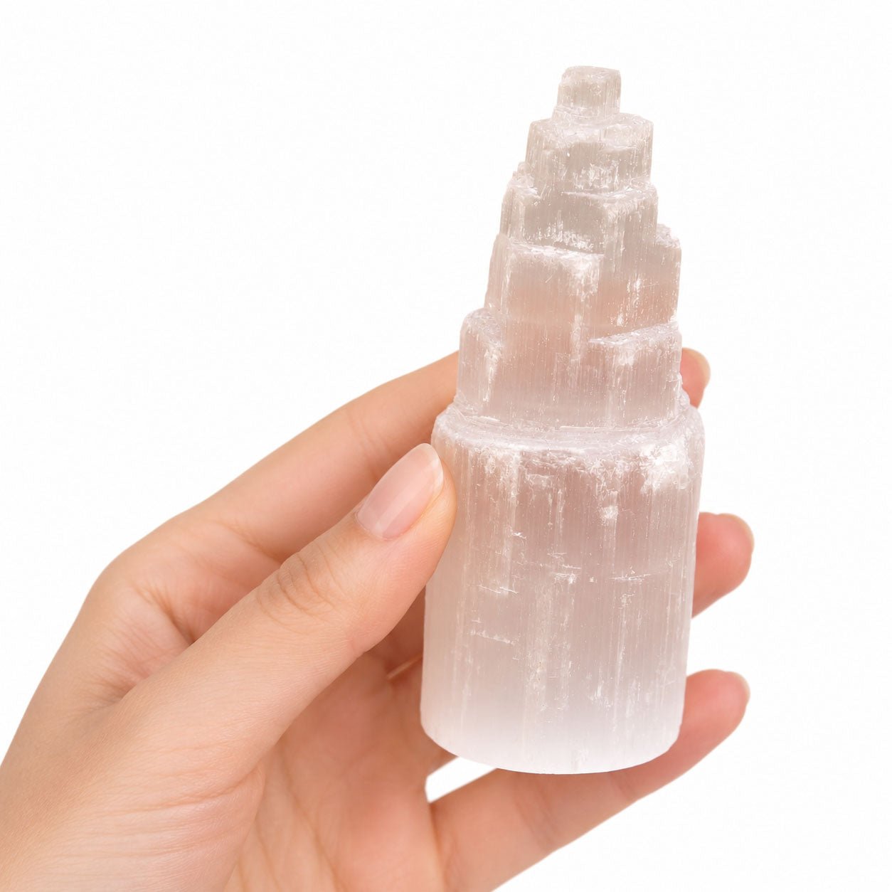 Hand holding a selenite tower crystal against a white background